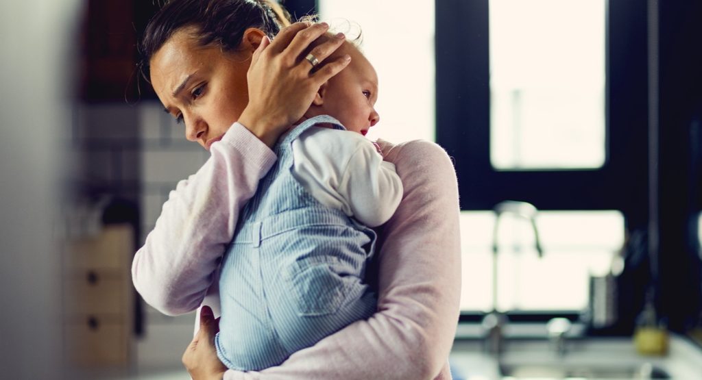 Mother holding her newborn while coping with postpartum depression and emotional stress after childbirth.