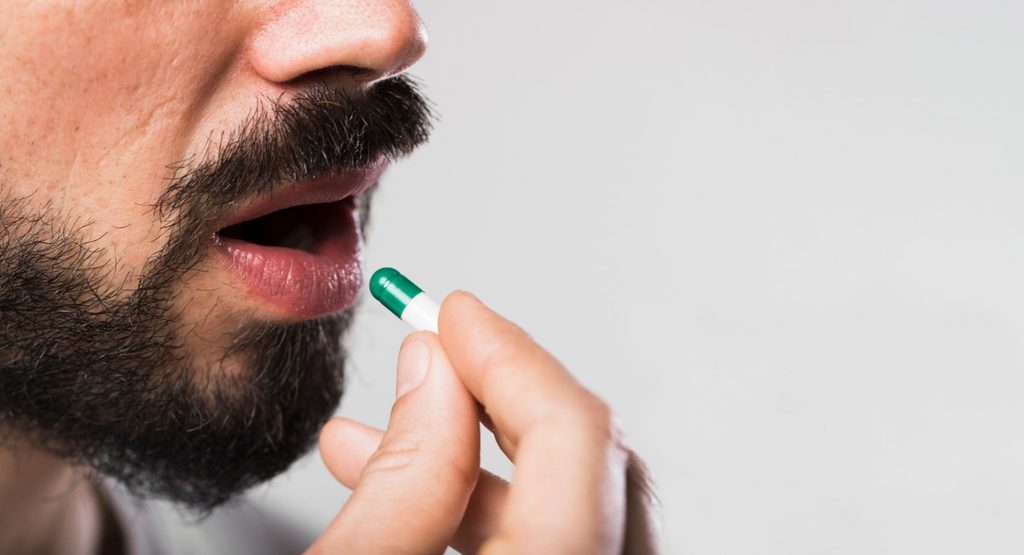 Man taking a psychiatric medication capsule to manage mental health symptoms and medication side effects.